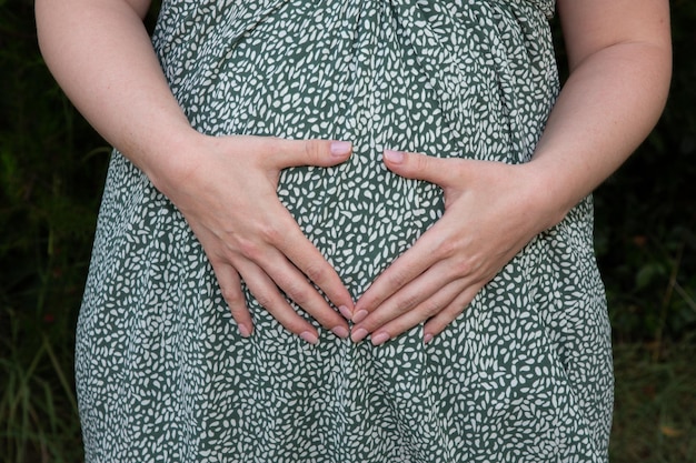 Ręce kobiety w ciąży robią palec serca w brzuchu