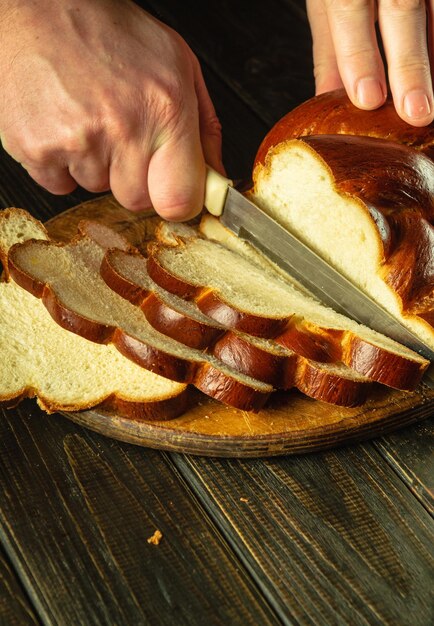 Ręce kucharza nożem wycinają świeży chleb pszenny lub kalach na kuchennej desce do cięcia Zdrowe jedzenie lub koncepcja gotowania