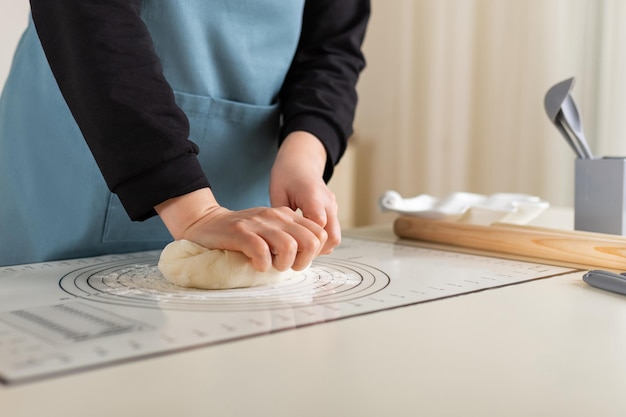 Ręce kucharza wyrabiają ciasto pszenne na gumowej macie kuchennej z różnymi oznaczeniami dla ułatwienia użytkowania