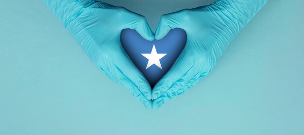 Ręce lekarzy w niebieskich rękawiczkach chirurgicznych, które sprawiają, że słyszysz symbol kształtu z flagą somalii