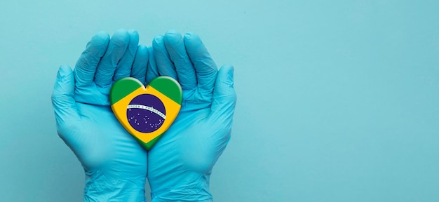 Ręce lekarzy w rękawiczkach chirurgicznych, trzymające serce z flagą Brazylii
