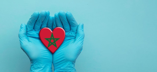 Ręce lekarzy w rękawiczkach chirurgicznych, trzymające serce z flagą Maroka