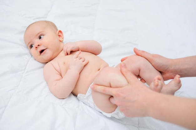 Ręce mamy trzymają nogi dziecka przy jego brzuszku. Masaż noworodka przeciw wzdęciom i kolkom.