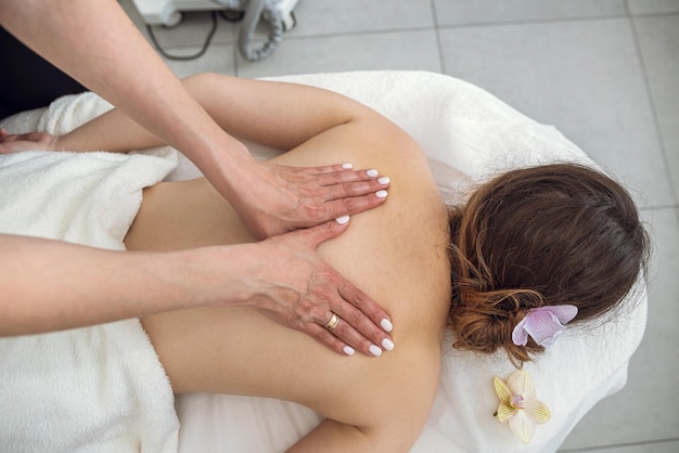 Ręce masażystki pracujące masując plecy w młodej pięknej kobiecie klientce w salonie spa