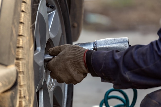 Zdjęcie ręce mechanika samochodowego odkręcającego nakrętki pneumatycznym kluczem udarowym w sezonie kół samochodowych