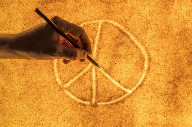 Ręce mężczyzn rysują na piasku międzynarodowy symbol pokoju. pojęcie pokoju i dobra