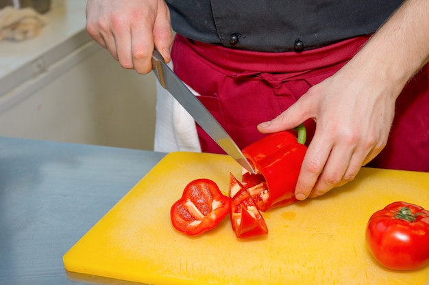 Ręce Mężczyzny Cięcia Dojrzałych Pomidorów W Plasterki Na Stole. Mąż W Kuchni Przygotowuje Sałatkę. Ręka Krojenie świeżego Pomidora Ogrodowego Z Dużym Nożem Kuchennym
