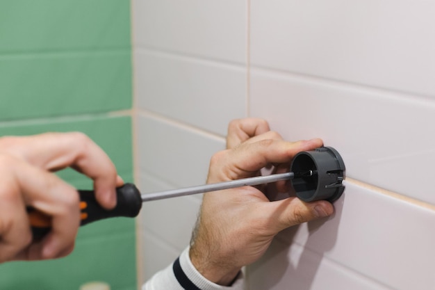 Ręce mężczyzny montują plastikowy element uchwytu prysznica wkręcają gwóźdź śrubokrętem, aby przymocować go do wykafelkowanej ściany w łazience Prace remontowe w łazience Brud po renowacji
