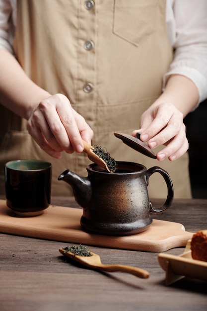 Ręce mężczyzny parzącego herbatę w ceramicznym garnku przy kuchennym stole
