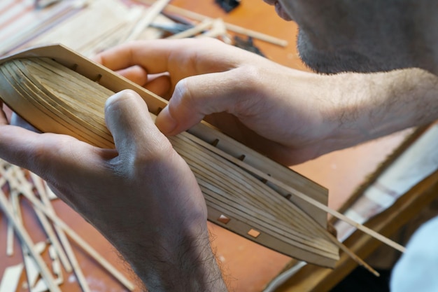 Ręce mężczyzny sklejające detale ze sklejki do modelu statku za pomocą kleju trzymającego palcami Proces budowania zabawkowego statku