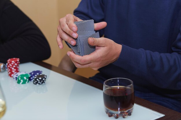 Ręce mężczyzny tasują karty w grze w pokera Karty z żetonami szklanka whisky na stole z odbiciem Klub pokerowy