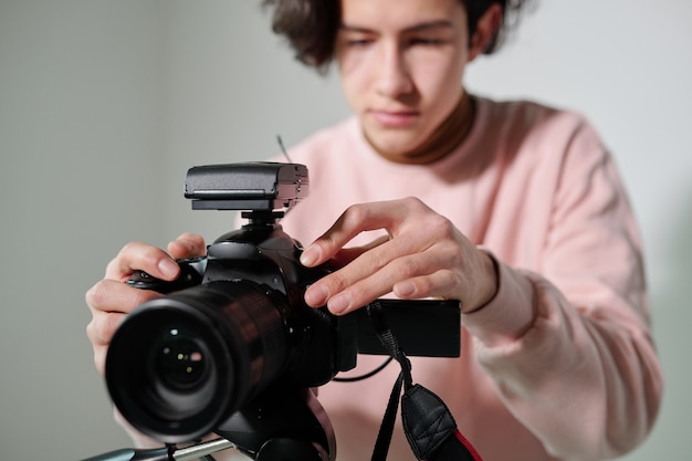 Ręce młodego kamerzysty w pudrowo-różowej bluzie regulujące sprzęt video podczas przygotowań do zdjęć