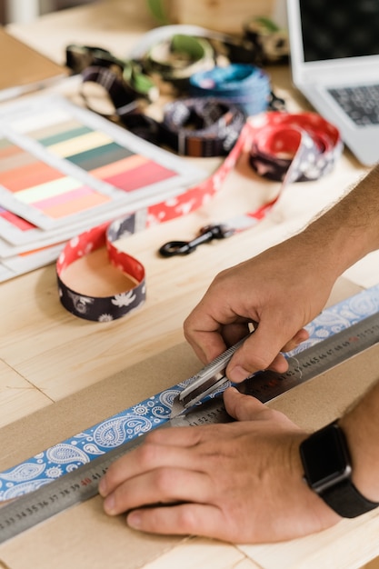 Zdjęcie ręce młodego kreatywnego projektanta używającego ręcznych narzędzi podczas przygotowywania dekoracyjnych elementów do ręcznie robionych obroży dla zwierząt