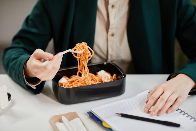 Ręce młodej współczesnej bizneswoman mającej smaczny chiński wok w pudełku na lunch w środku dnia pracy, siedząc przy biurku