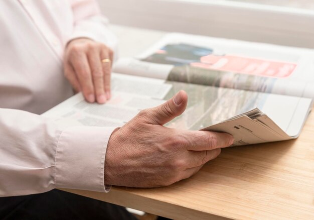 Ręce nierozpoznawalnego starca czytającego gazetę na drewnianym stole