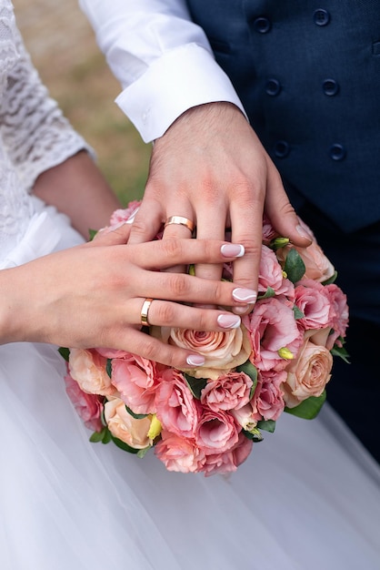 Ręce pary młodej z obrączkami na tle bukietu róż