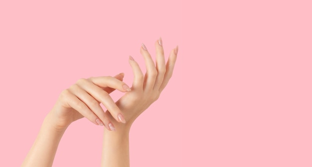 Ręce pięknego, zadbanego, beżowego marmurkowego lakieru do paznokci na różowym tle