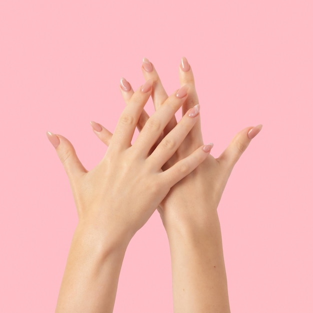 Ręce pięknego, zadbanego, beżowego marmurkowego lakieru do paznokci na różowym tle