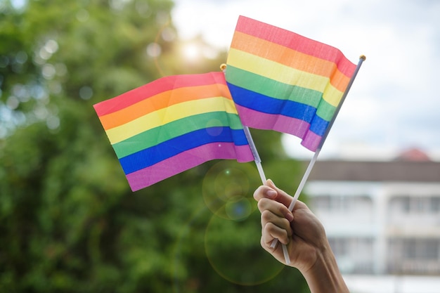 Ręce pokazujące tęczową flagę LGBTQ na zielonym tle przyrody Wsparcie dla lesbijek gejów, osób biseksualnych, osób transpłciowych i queer, oraz koncepcja miesiąca dumy