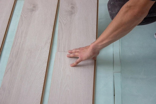 Ręce pracowników układają drewnianą podłogę laminowaną. Remont domu z drewnianymi podłogami z pomiarami. selektywne skupienie