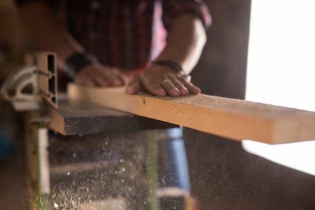 ręce prawdziwego stolarza piłującego kawałek drewna piłą stołową w stolarni