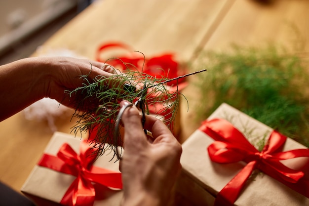 Ręce przyciętej nierozpoznawalnej kobiety pakującej prezent świąteczny, ekologiczne opakowania prezenty z papieru kraft, kobieta pakująca prezent świąteczny, pudełko upominkowe