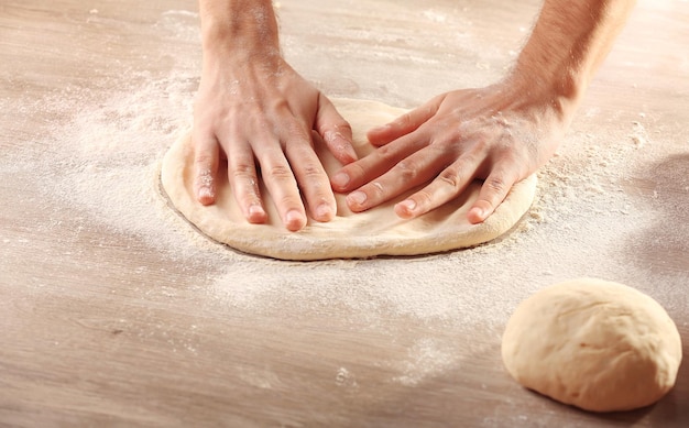 Ręce przygotowujące podstawę ciasta na pizzę na drewnianym stole zbliżenie