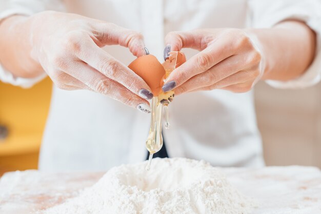 Ręce rozbijające jajo kurze na mąkę na stole