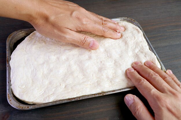 Ręce rozciągające wyrośnięte ciasto na patelni do pieczenia pizzy lub chleba