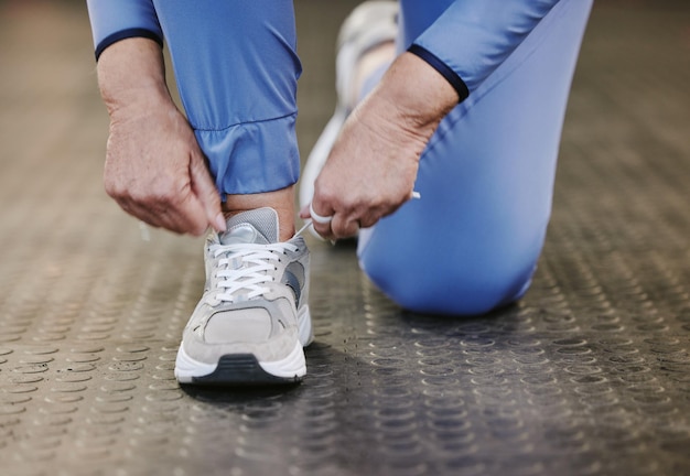 Ręce sportowe i wiązanie butów na siłowni, aby rozpocząć trening lub ćwiczenia dla dobrego samopoczucia Fitness sportowiec zdrowy lub starsza kobieta wiążąca trampki lub sznurowadła do obuwia, aby przygotować się do ćwiczeń lub biegania