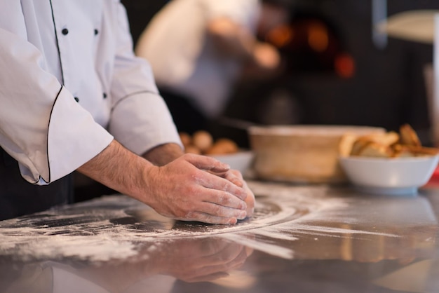 ręce szefa kuchni przygotowujące ciasto do pizzy na posypanym mąką zbliżenie stołu