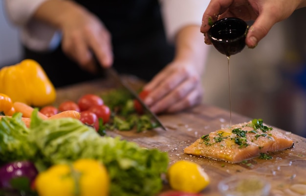 Ręce Szefa Kuchni przygotowujące filet z marynowanego łososia do smażenia w kuchni restauracji