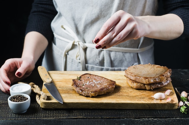Ręce szefa kuchni solone stek wołowy na drewnianej desce do krojenia.