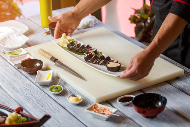 Ręce trzymają talerz z sushi. Roladki sushi na długim talerzu. Futomaki bułki serwowane w restauracji. Najlepsze danie z menu.
