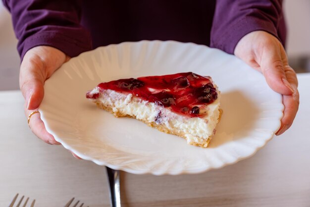 Zdjęcie ręce trzymające cheesecake z wierzchołkiem wiśniowym i drewnianym tłem