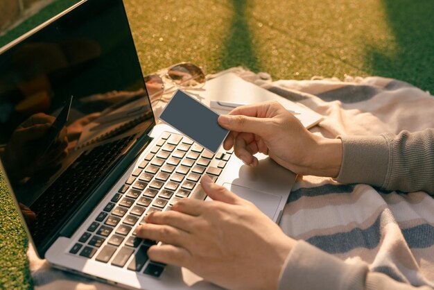 Ręce trzymające kartę kredytową i używające laptopa na naturalnym letnim tle