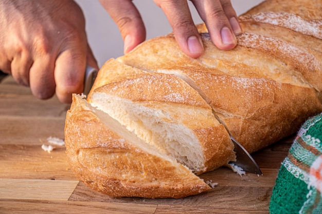 Ręce trzymające nóż i krojące chleb na kromki do podania