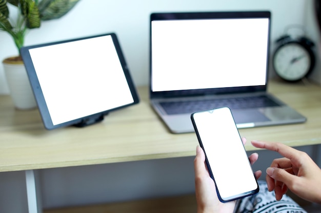 Zdjęcie ręce trzymające pusty biały ekran telefonu komórkowego z laptopem i tabletem na stole w o