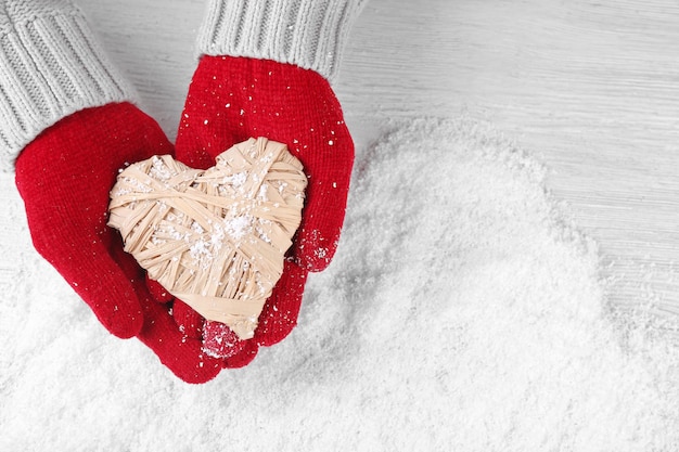 Ręce w ciepłych czerwonych rękawiczkach trzymające wiklinowe serce na śnieżnym tle