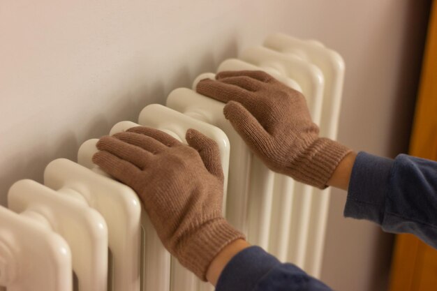 Ręce w ciepłych rękawiczkach w pobliżu grzejnika w pokoju
