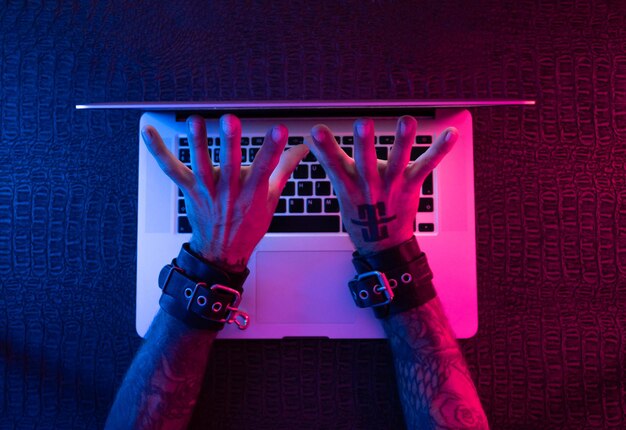 Ręce w kajdankach bdsm z laptopem w neonowym świetle