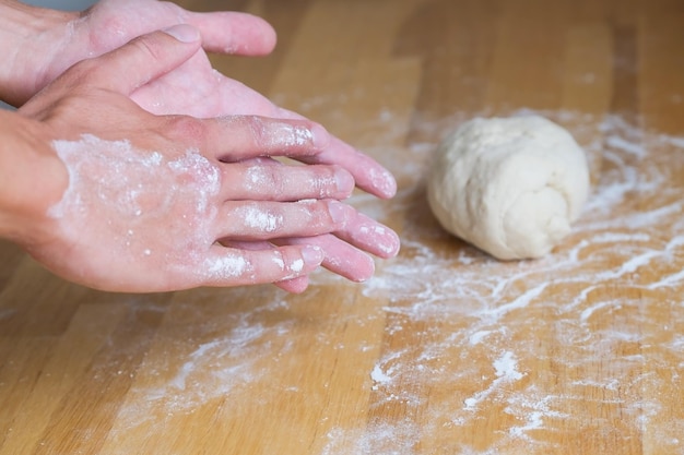 Ręce w mące na kawałku ciasta podczas robienia pizzy i pieczenia