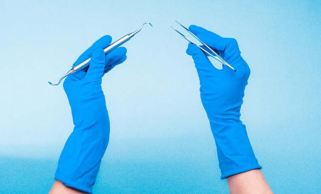 Ręce w niebieskich rękawiczkach trzymające narzędzia dentystyczne na jasnoniebieskim tle
