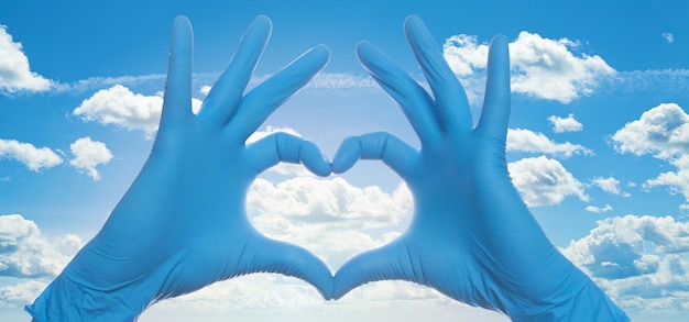 Ręce w rękawiczkach lekarza tworzą serce na tle chmur nieba
