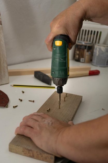 ręce z elektrycznym śrubokrętem wkręcającym śruby w drewno