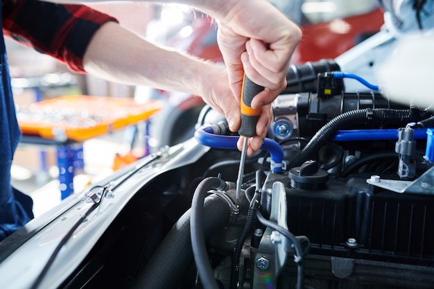 Ręce z mechanikiem za pomocą śrubokręta podczas mocowania śrub w silniku samochodu podczas prac naprawczych