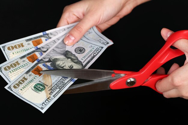 Zdjęcie ręce z nożyczkami wycinające banknoty dolara na czarnym tle