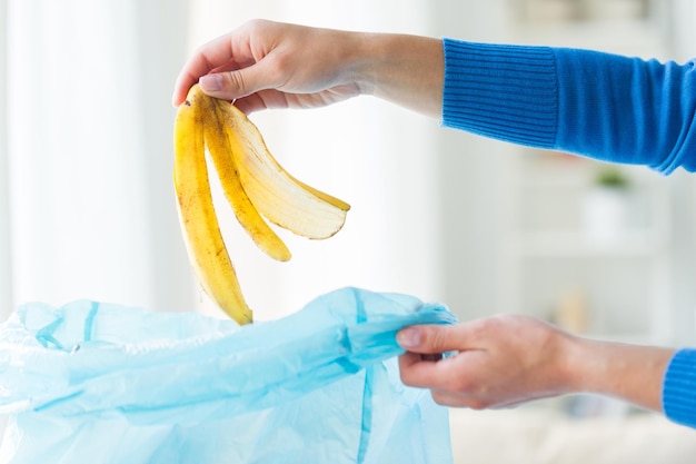 recykling, marnotrawstwo żywności, śmieci, koncepcja środowiska i ekologii - zbliżenie ręki wkładającej skórkę banana do worka na śmieci w domu