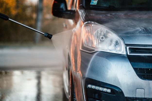Ręczna myjnia samochodowa z białą pianką mydlaną na karoserii Mycie samochodu wodą pod wysokim ciśnieniem