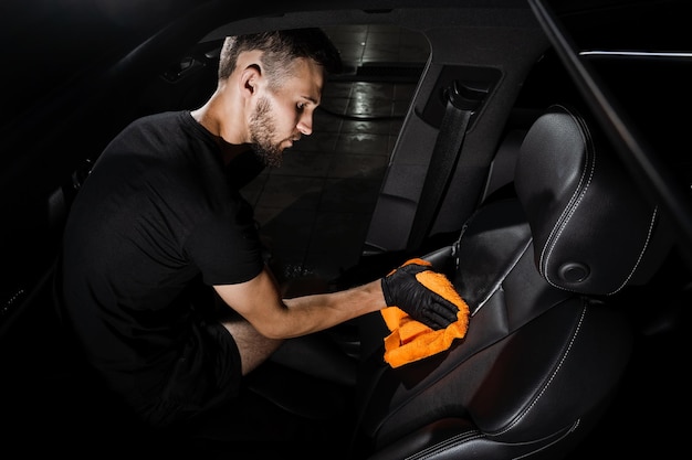 Ręczne suszenie skórzanego fotela wnętrza samochodu przy użyciu mikrofibry w detalu autoserwis Pracownik sprzątający suche wnętrze samochodu